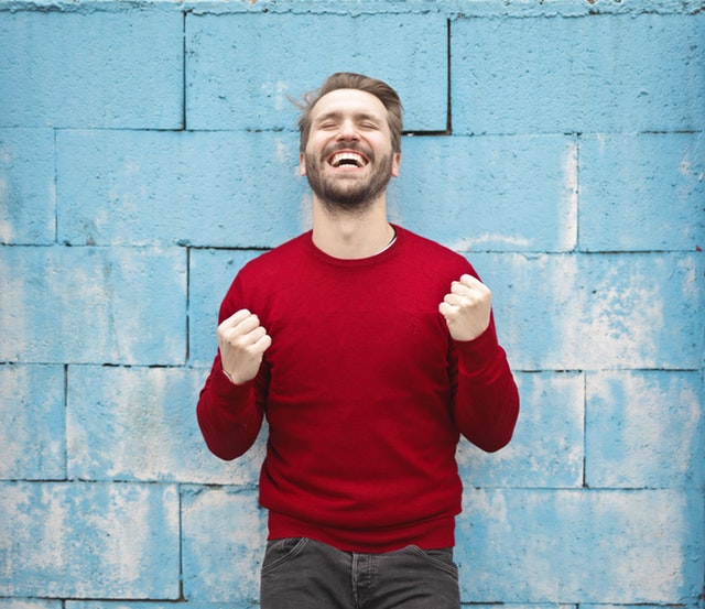 The benefits of hearing aids Hppy man standing in front of a wall